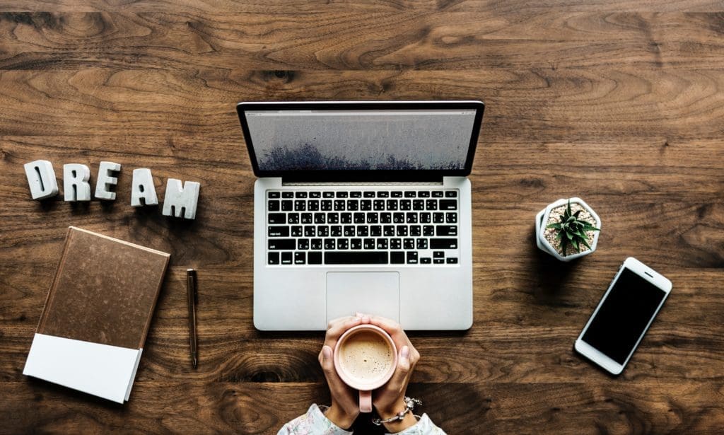 desk with a laptop, woman holding a latte and the word dream